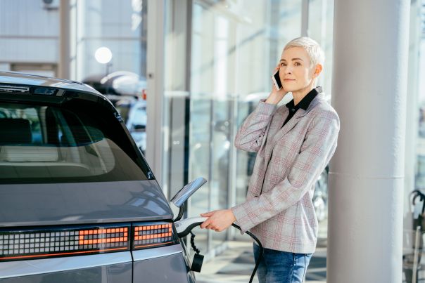 A person plugging a charger into an electric vehicle while speaking on their mobile phone.